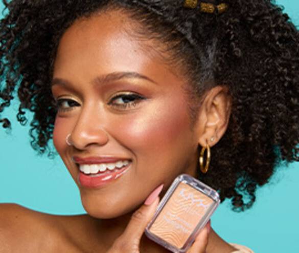 A smiling woman with curly hair and gold accessories holds a NYX makeup product against a bright teal background.